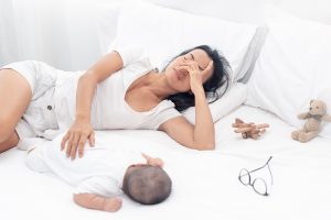 Photo of a first time mom resting in bed with her sleeping baby. She is experiencing symptoms of postpartum after giving birth. She and her partner think she should look for postpartum therapy in Chicago, IL 60301 | 60302